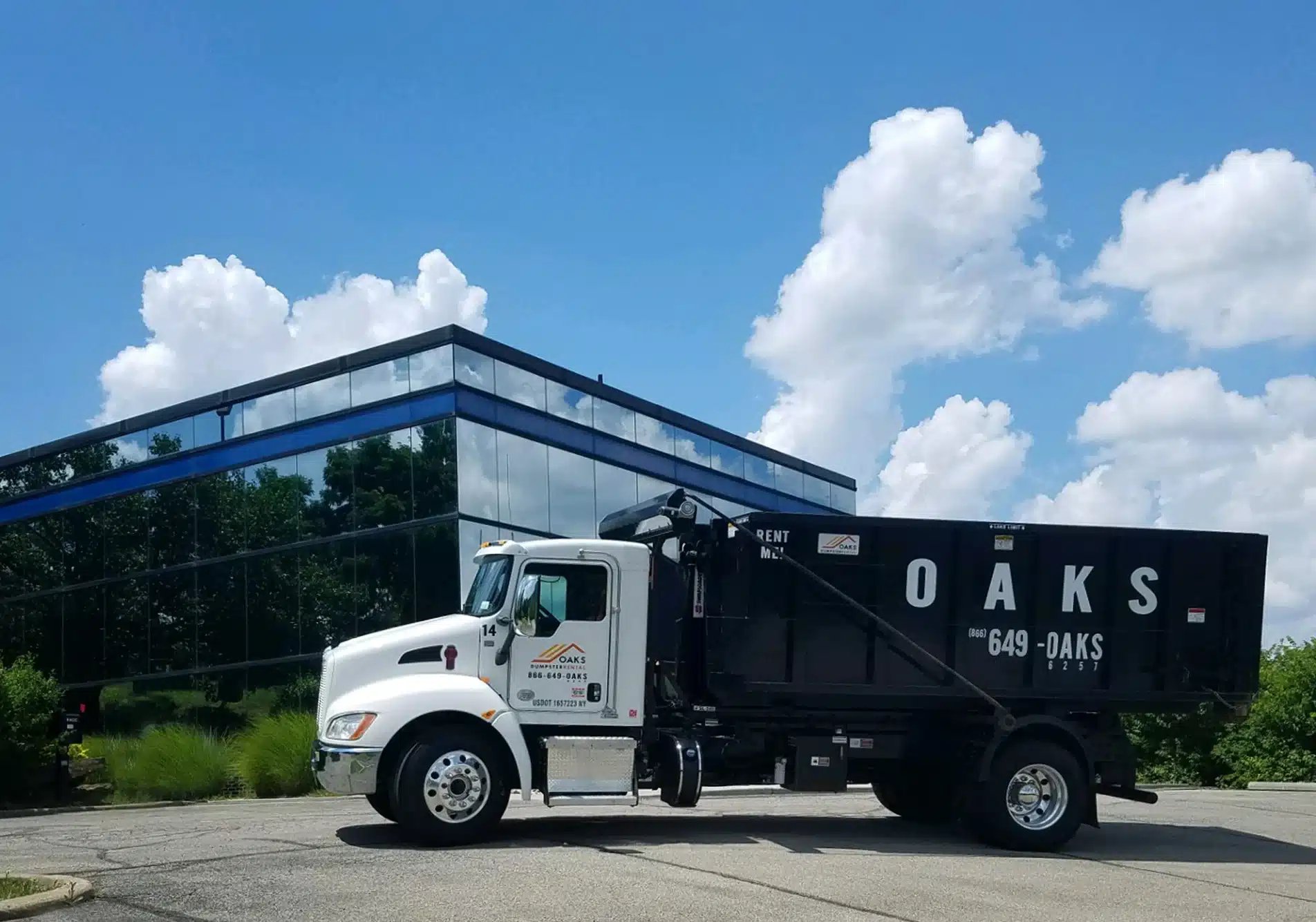 A white truck with a black dumpster parked outside.
