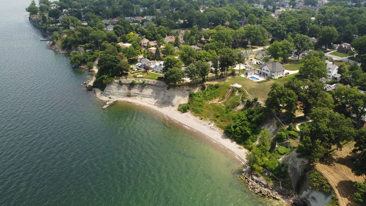 Aerial view of a beach with a residential area. The water is calm and green.