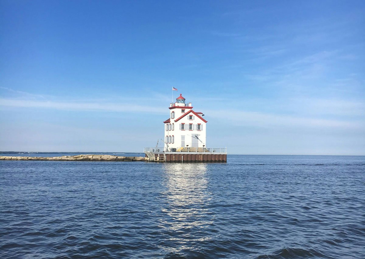 a white lighthouse on a pier. The lighthouse has a red roof.