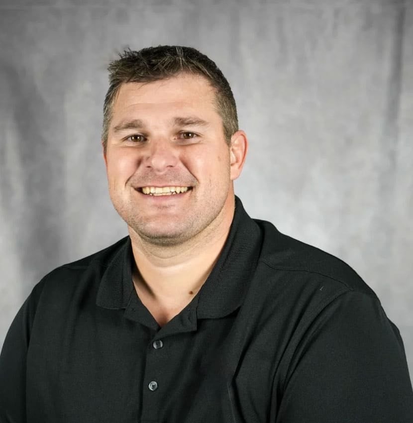 A man wearing a black polo shirt smiles at the camera.