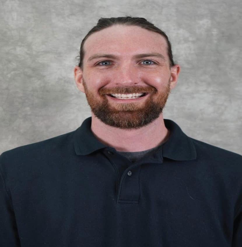 A man with a beard smiles at the camera. He is wearing a black polo shirt.