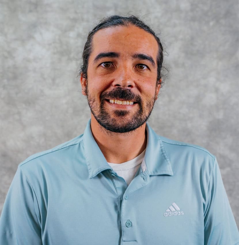 A man with a beard and mustache wearing a light blue Adidas polo shirt. He is smiling at the camera.