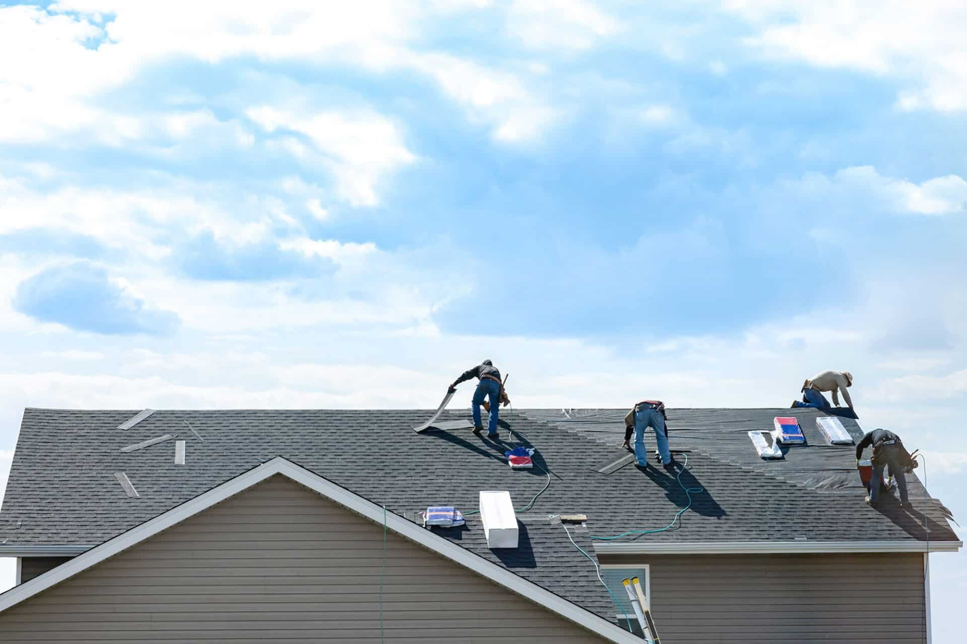 Workers installing roof shingles on a house. Roofing construction site.