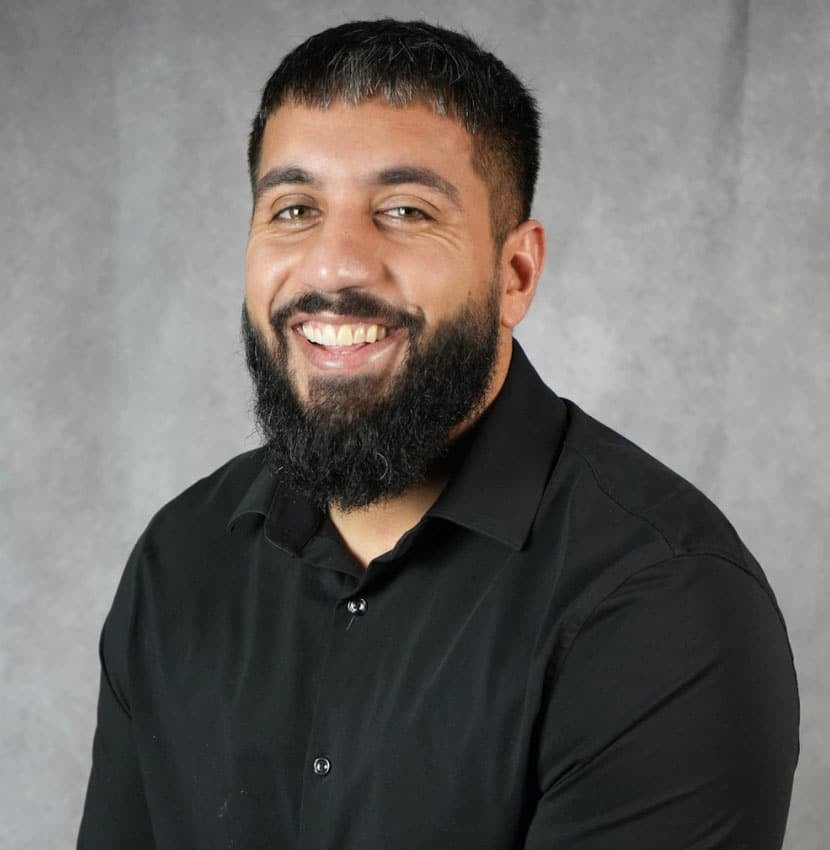 A man with a beard smiling at the camera. He is wearing a black shirt.