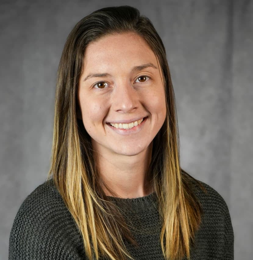 Portrait of a woman with long brown hair. She is smiling and looking at the camera.