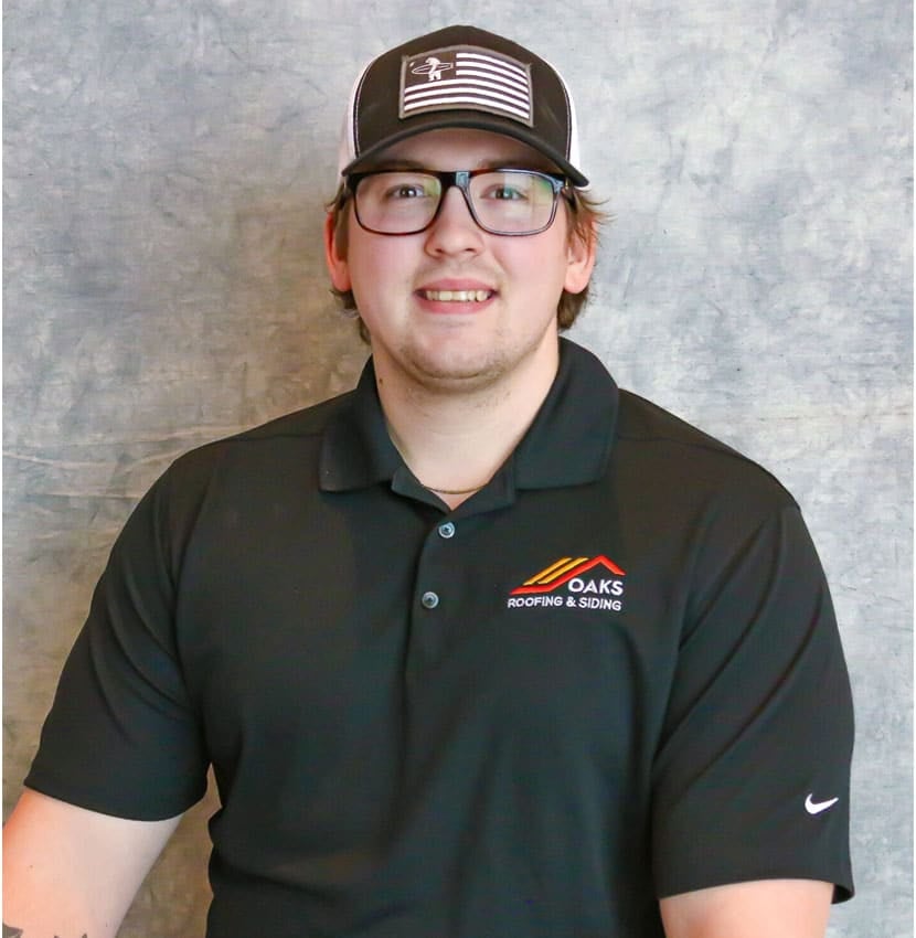 A young man wearing a black polo shirt and baseball cap. He is smiling at the camera.