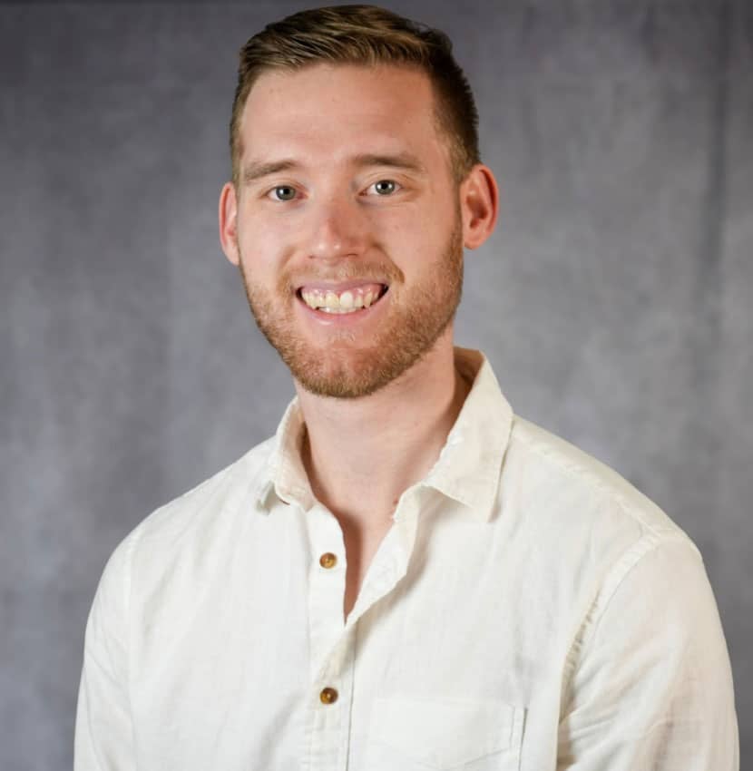 A smiling young man with short brown hair and a white button down shirt.