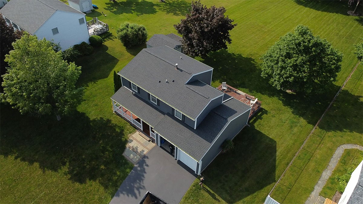 A two-story house with a grey roof and green lawn. The house has a driveway and trees around it.
