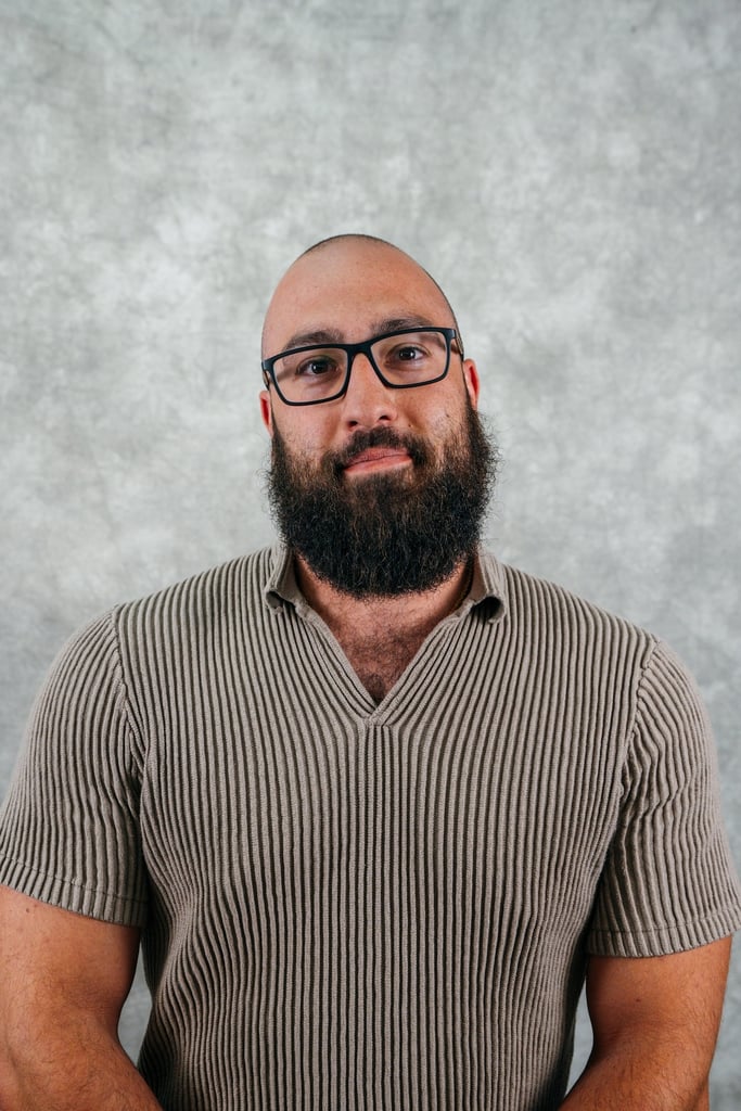 Man with beard and glasses looking forward. He is wearing a striped shirt.