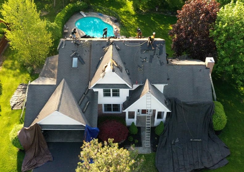 A large house with a pool and trees. Roofing work in progress.
