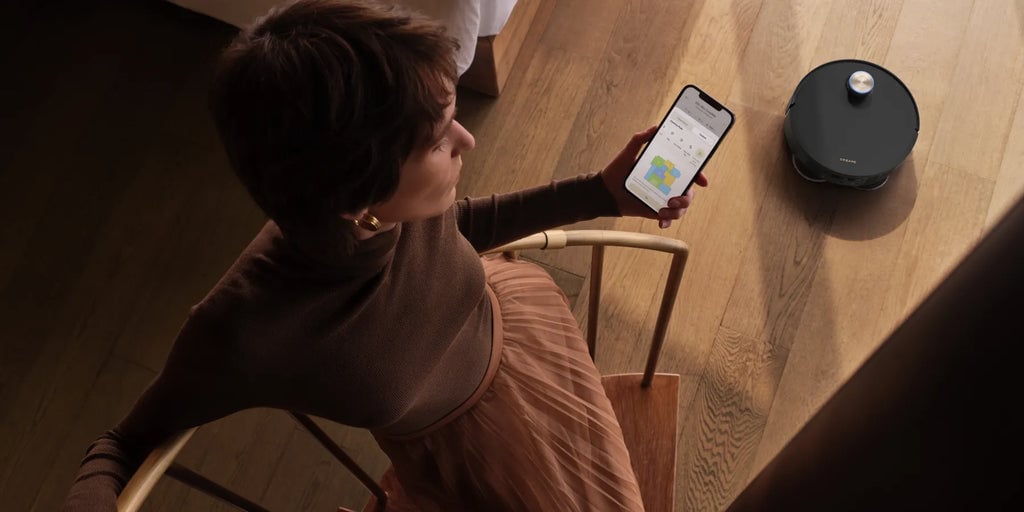 Person controlling Dreame X50 Ultra robot vacuum with a smartphone app.
