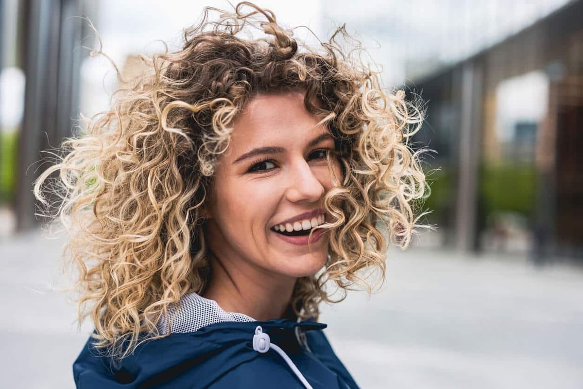 How to Use Leave In Conditioner for Curly Hair. Portrait of laughing young woman outdoors stock photo.