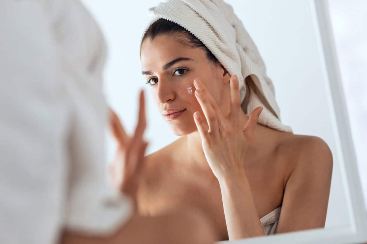 Beauty Blog Best Acne Spot Treatment Products. Beautiful young woman caring of her skin while putting on cream looking at mirror at home. stock photo.