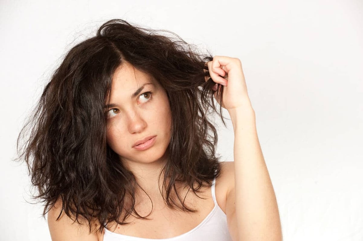 Best Shampoo for Coarse Hair. Woman clutching wavy dark hair over a white background stock photo