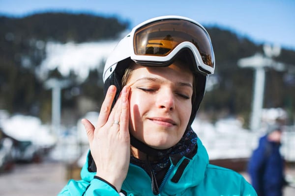 Why You Need Serious Skin Protection for Skiing. Young adult woman rubbing sunscreen stock photo
