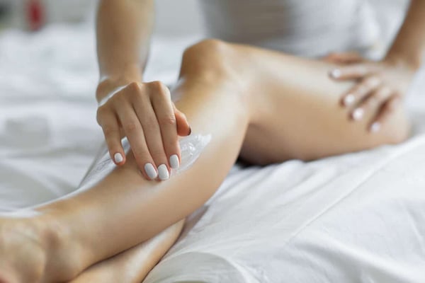 Top Body Lotion for Dry Skin. Woman applying body lotion on her legs at her bedroom. stock photo