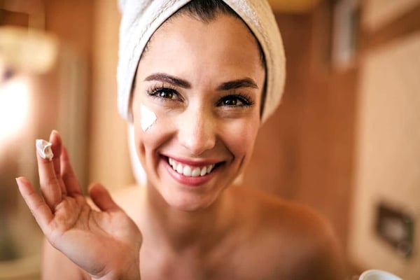 Our Top Moisturizers with SPF Protection. Young happy woman applying moisturizer on her face in the bathroom.