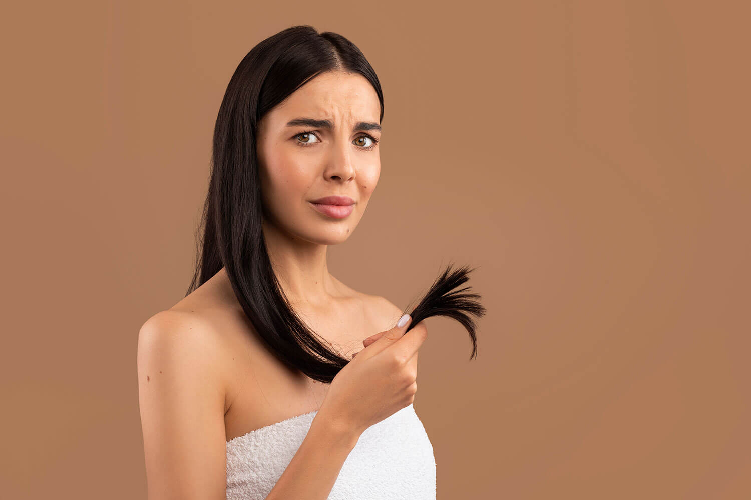 How to Fix Dull Hair. Unhappy brunette woman showing her dull long hair, beige background