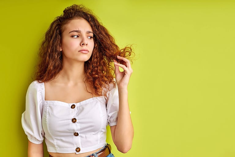 Effective Split Ends Treatment Plan. thoughtful curly girl is looking at split ends of hair, examine it, want to cut out.