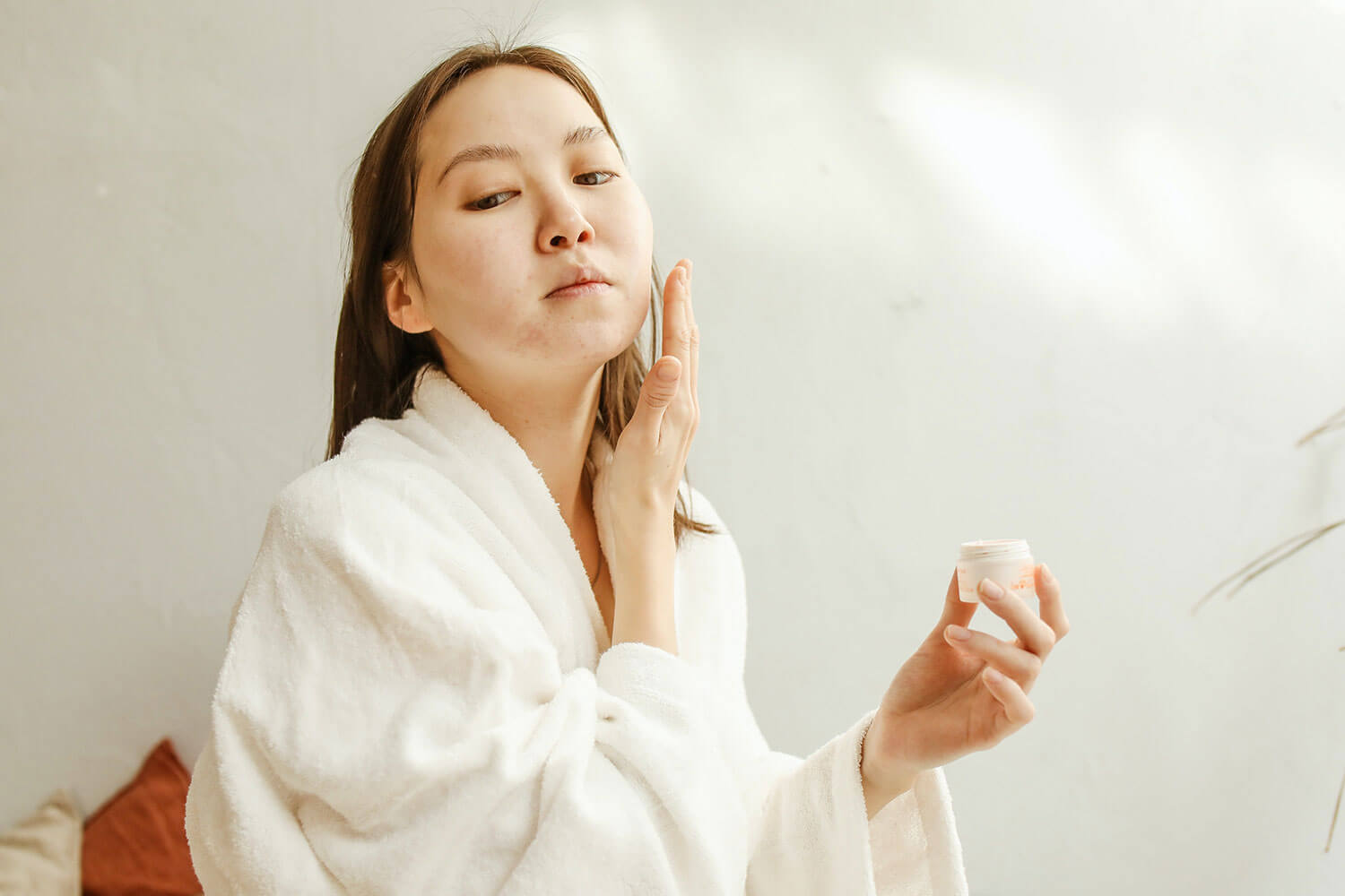 Building an Effective Acne Prone Skin Care Routine. Woman in White Bathrobe Putting on Skin Care Product on Her Face.
