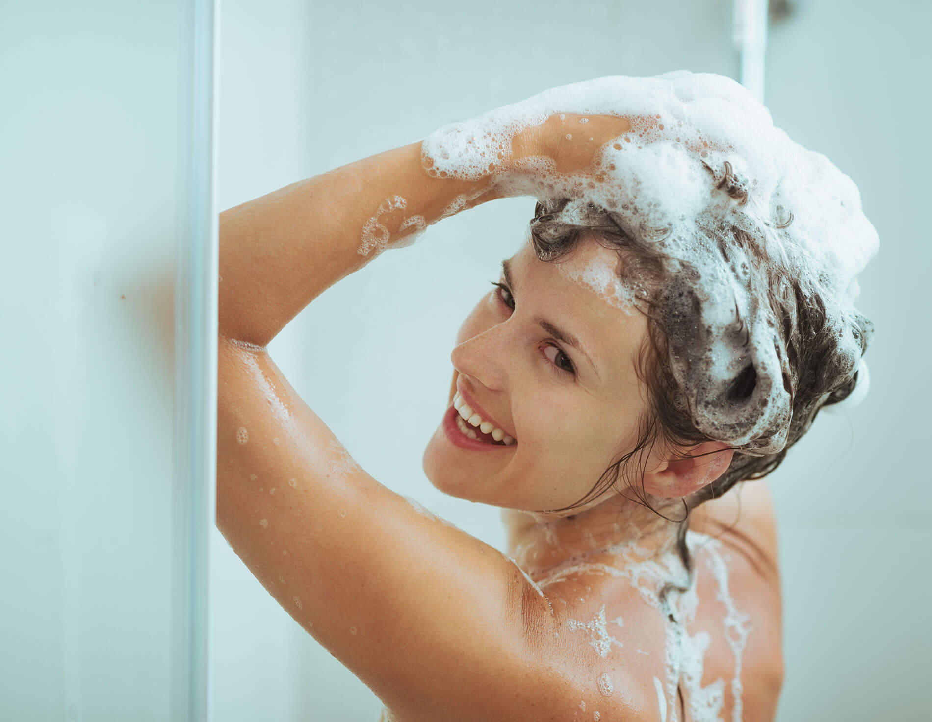 What Is a Clarifying Shampoo and How Do I Use It? Smiling young woman washing head with shampoo.