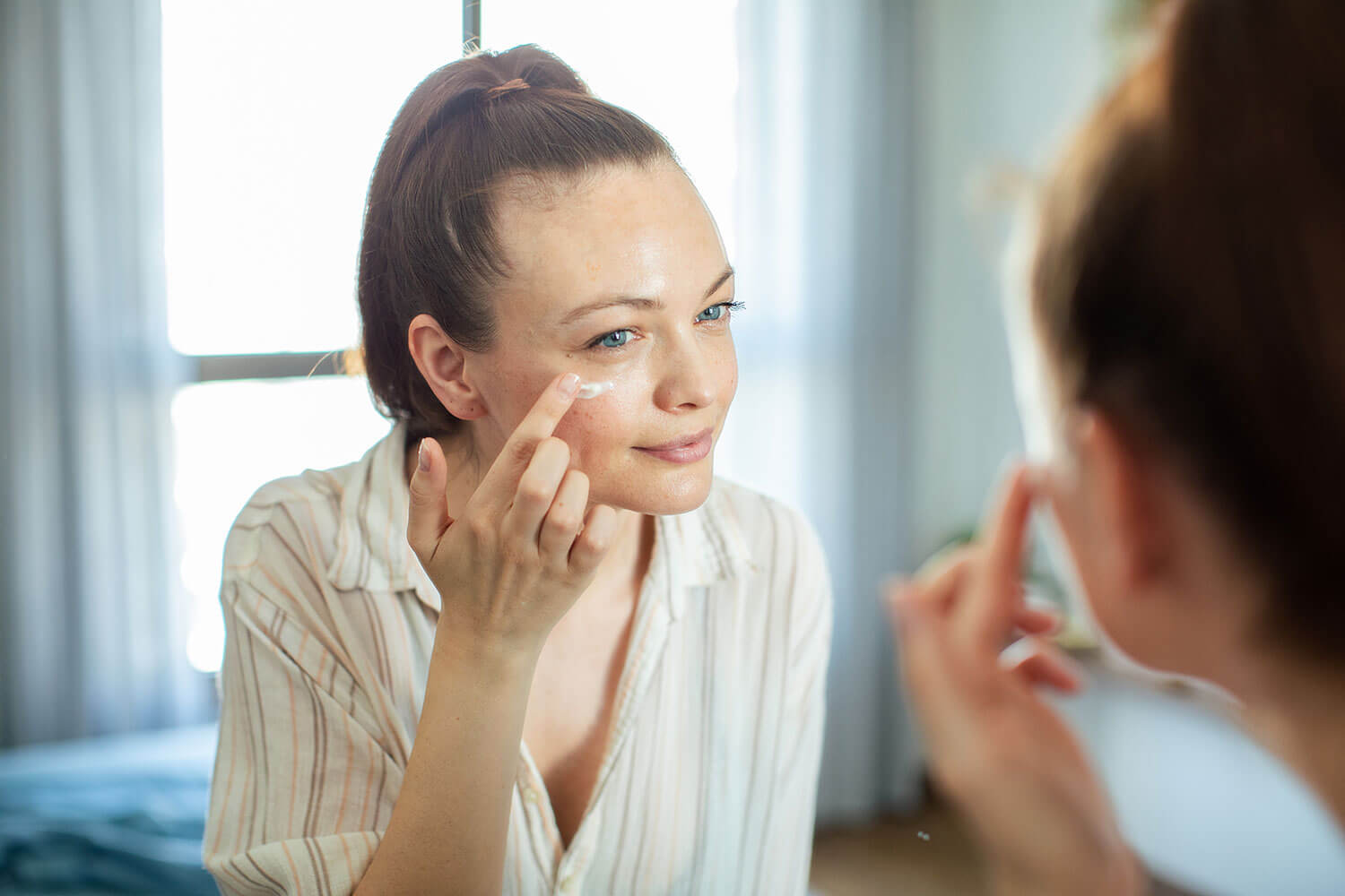 Essential Tips For Choosing the Best Night Cream. Young woman putting on makeup while looking in a mirror at home stock photo
