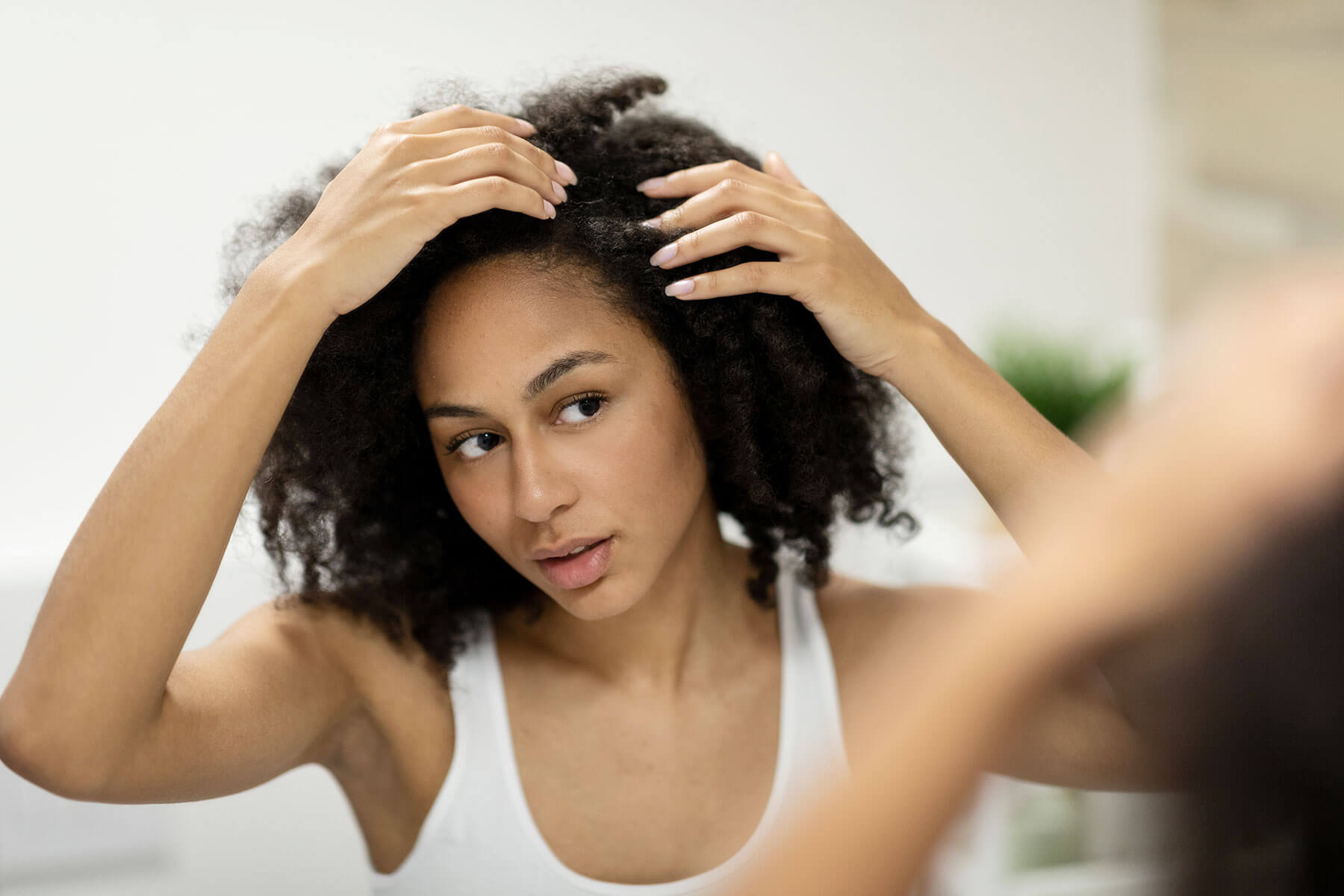 How to Get Rid of Dry Scalp. Portrait of a beautiful young woman examining her scalp and hair in front of the mirror, hair roots, color, grey hair, hair loss or dry scalp problem