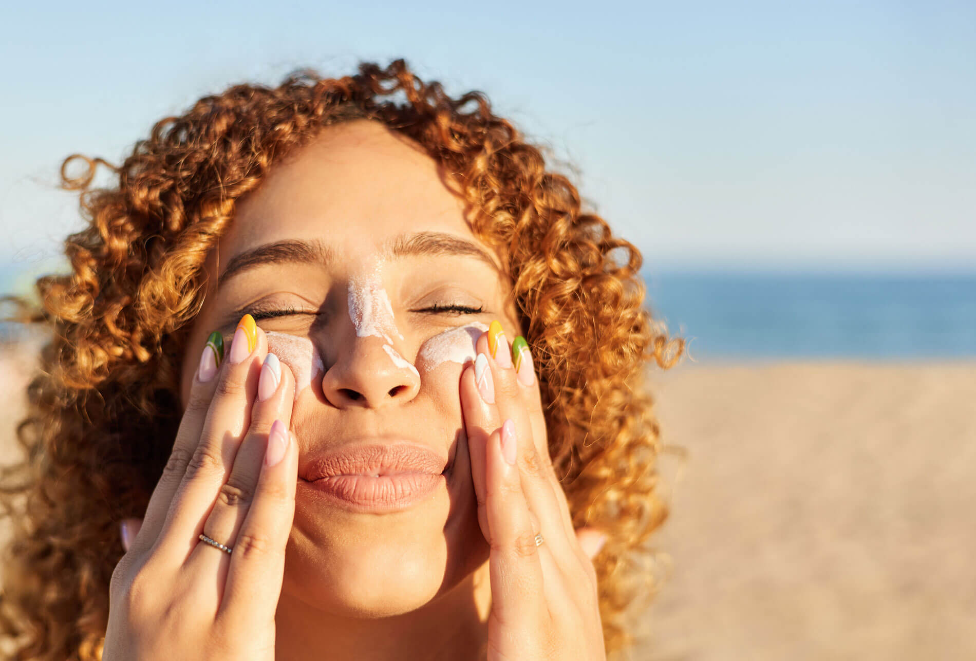 Best Sunscreen for The Face. Smiling happy woman applying sunscreen to her face on the beach at sunset. stock photo.