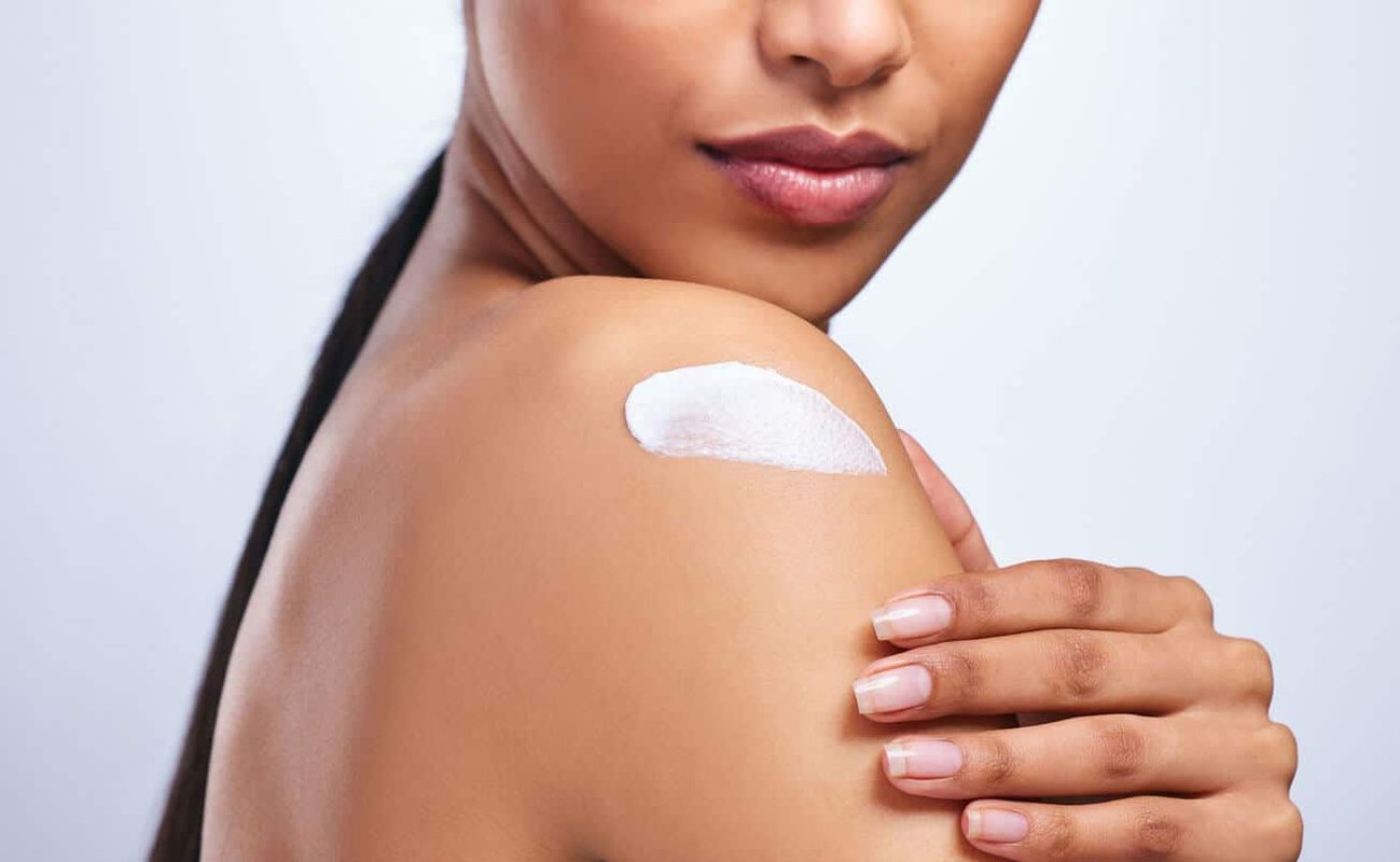 Beauty Blog Why Zinc Oxide Sunscreen is Your Best Choice. Cropped shot of an unrecognizable woman applying moisturiser to her shoulder against a grey background stock photo