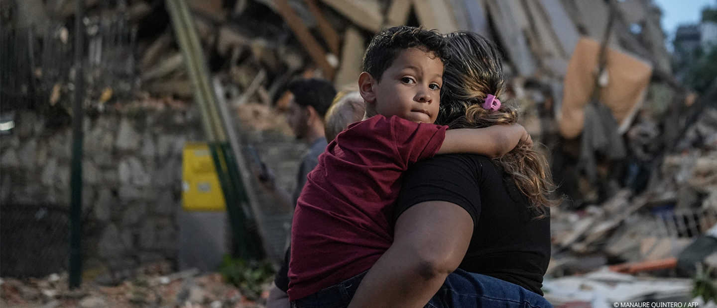 Ein Junge steht mit seiner Mutter vor den Trümmern des Erdbebens in Venezuela.
