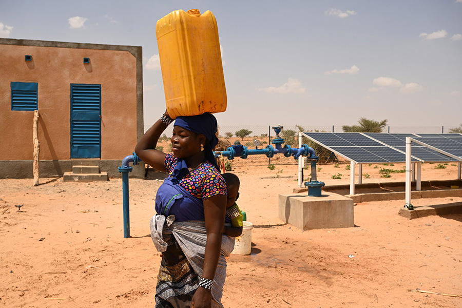 Im Niger trägt eine Frau Wasser von einem solarbetriebenen Brunnen nach Hause.