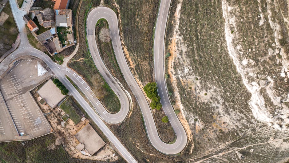 Aerial shot of a serpentine road in Peñafiel, Castilla y León, surrounded by rugged terrain.