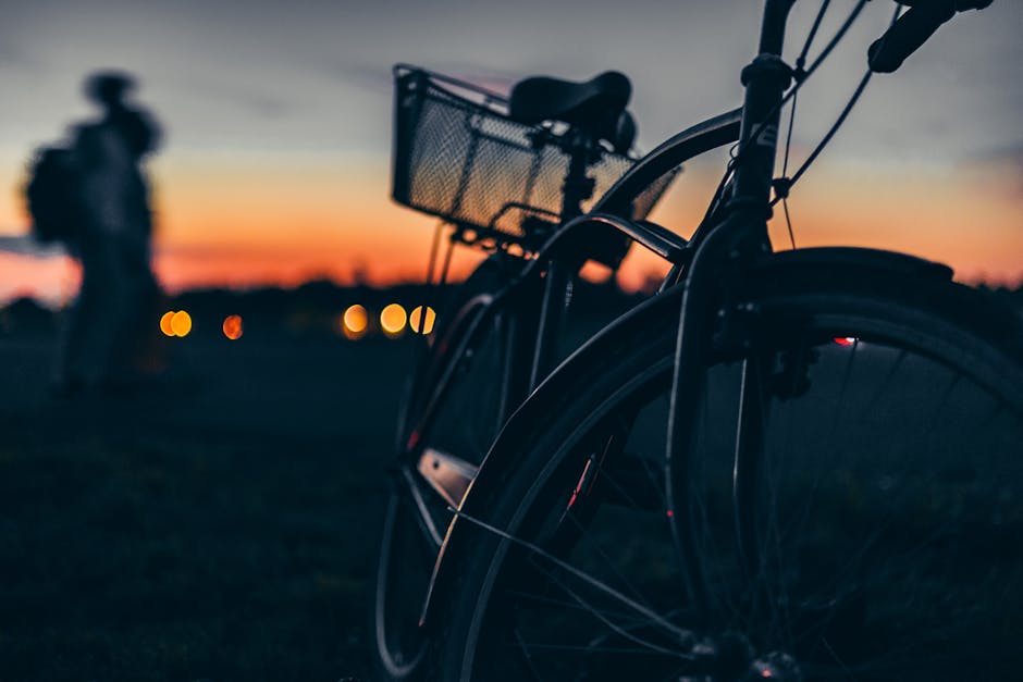 Silhouette of a bicycle at sunset with a blurry person in the background.