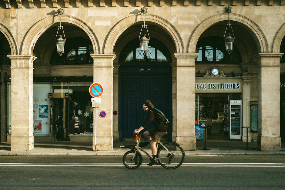 A cyclist riding past historic arches in Paris, showcasing urban life.