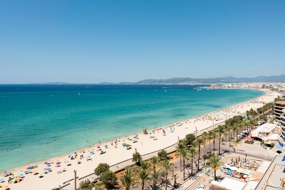 A breathtaking aerial view of Palma de Mallorca beach, showcasing crystal clear waters and a lively summer scene.