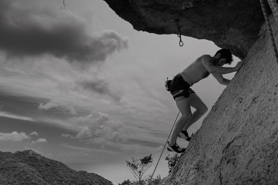 A monochrome image of a man rock climbing against a cloudy sky, showcasing strength and adventure.