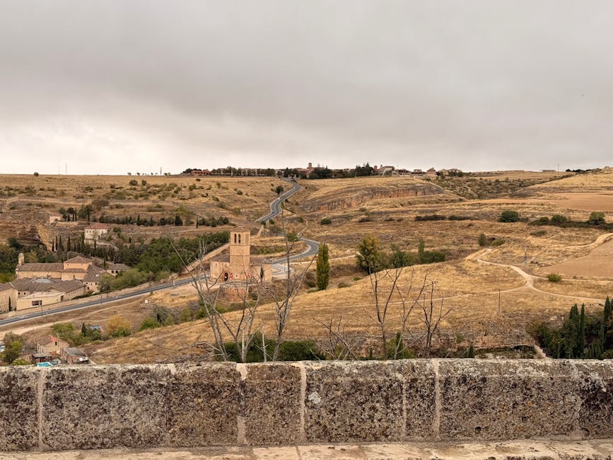 Scenic view of Segovia's rolling fields and historic architecture under a cloudy sky.