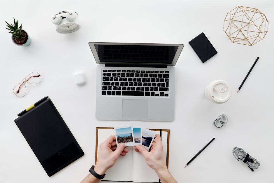 Flat lay of an organized workspace with a laptop, photos, and office supplies.