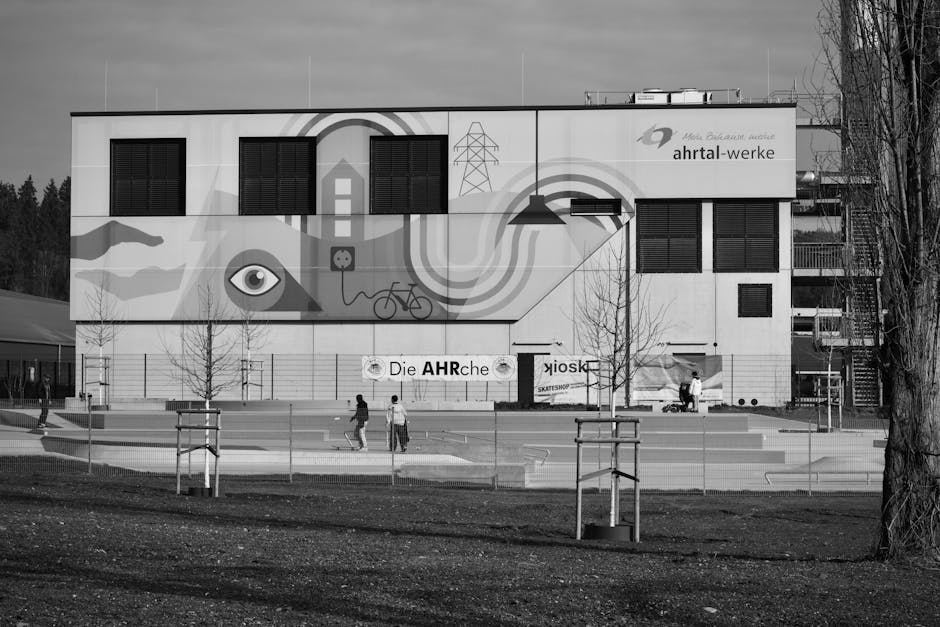 Black and white photo of a modern industrial building with a distinctive mural and people in front.
