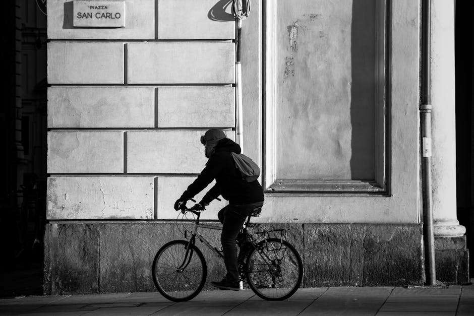A person cycling by a historic wall in Piazza San Carlo, Torino, captured in black and white.