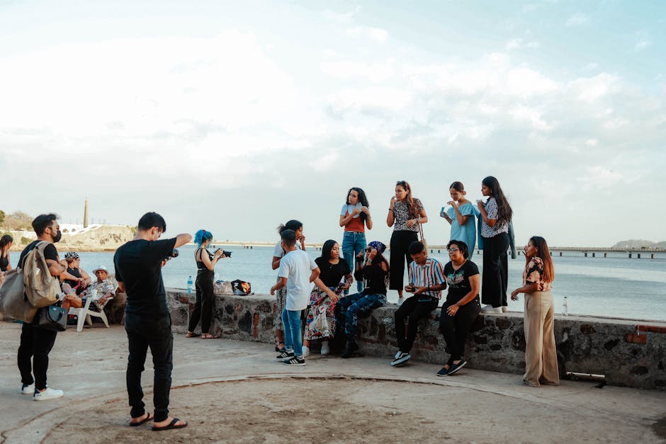 A diverse group of friends relaxing and taking photos by the seaside on a sunny day.