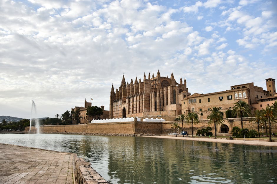 Stunning view of Cathedral de Mallorca by the tranquil waterfront under a cloudy sky.