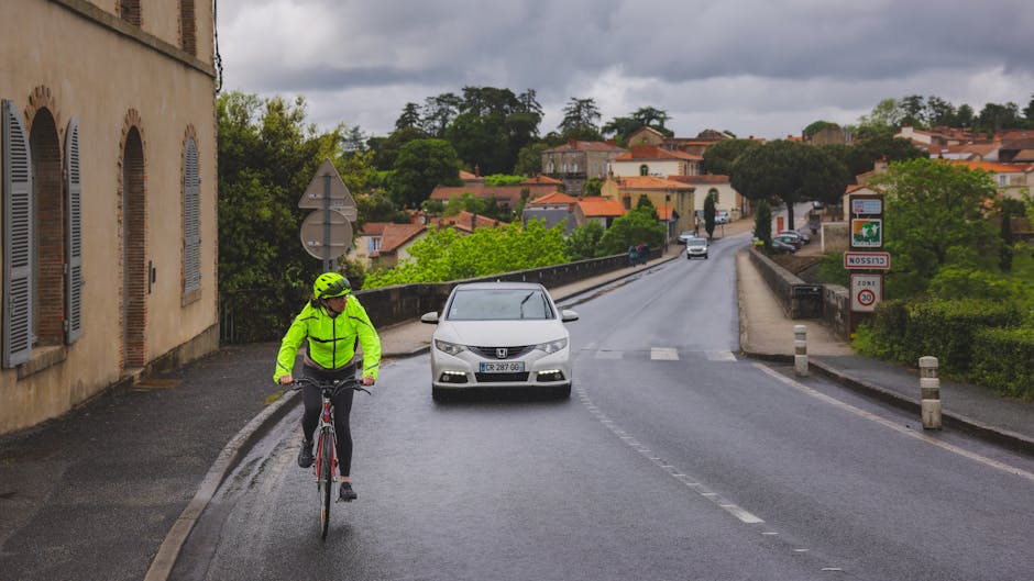 Cyclist in neon gear riding on a road in Clisson, France with scenic residential background.