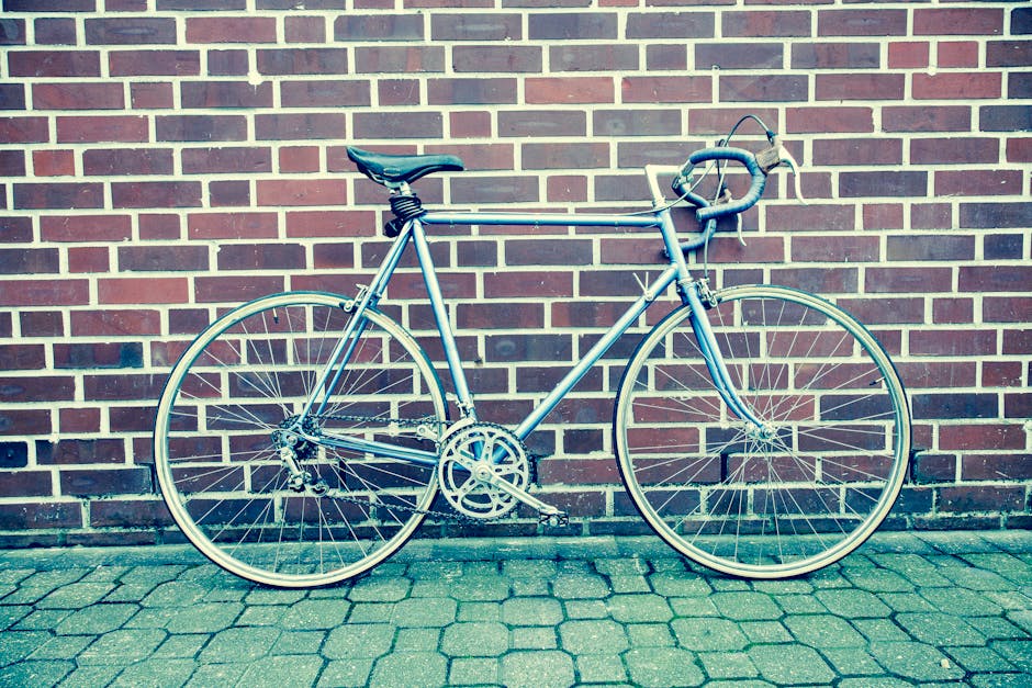 A classic racing bicycle leaning against a brick wall on a paved street.