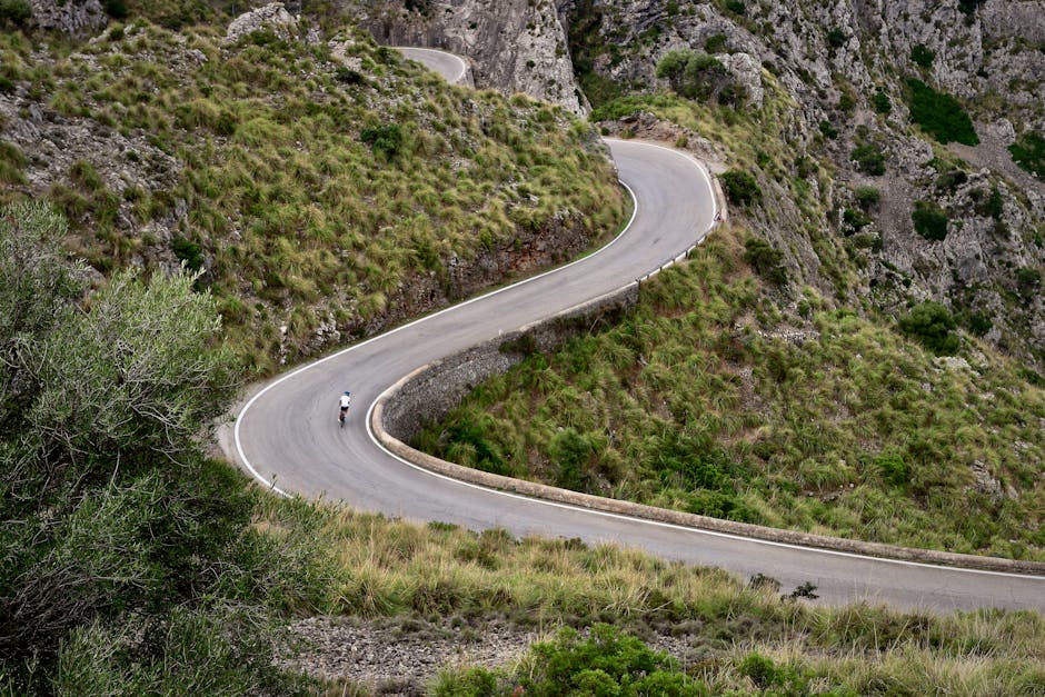 A lone cyclist navigates a winding mountain road amidst stunning natural scenery.