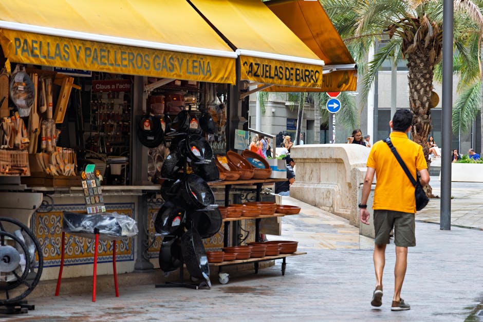 Vibrant street market in Spain featuring paella cookware under a yellow canopy.