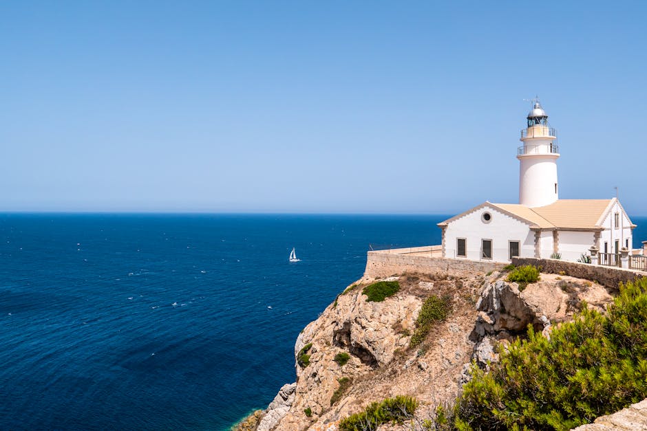 Breathtaking view of a lighthouse perched on Mallorca's rugged coastline overlooking the blue Mediterranean Sea.