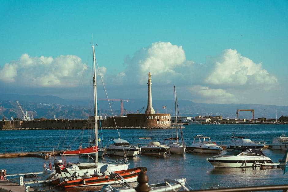 Skyline view of Messina harbor with moored boats and the iconic statue in the background.