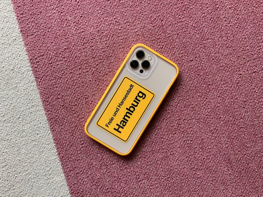 Smartphone with vibrant yellow case displaying 'Hamburg' on a textured pink carpet.