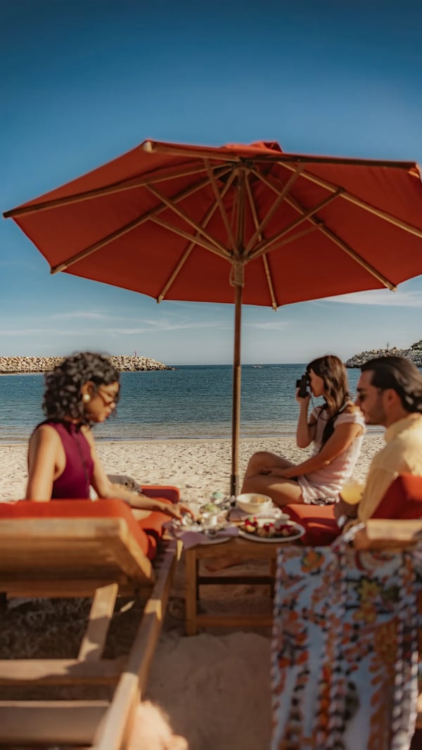 Friends sharing a meal under a red umbrella on the beach